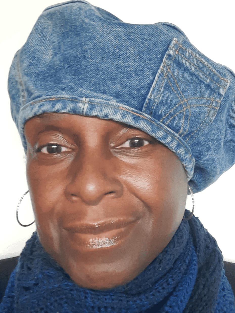Smiling woman wearing a blue denim beret and scarf, facing the camera against a plain light background.