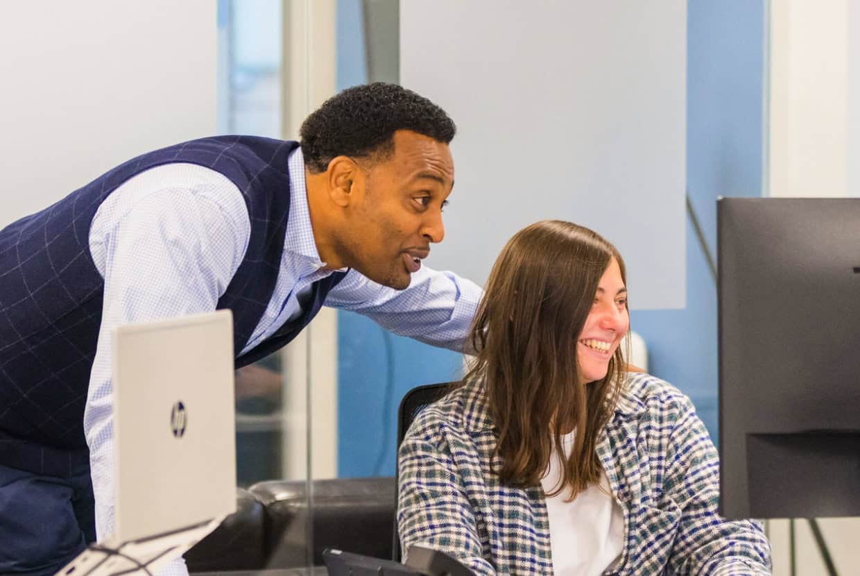 A man and woman smiling while looking at a computer screen in a modern office.